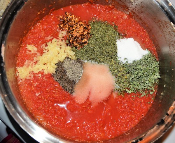 Dry ingredients poured into pureed tomatoes for making homemade spaghetti sauce in large stockpot