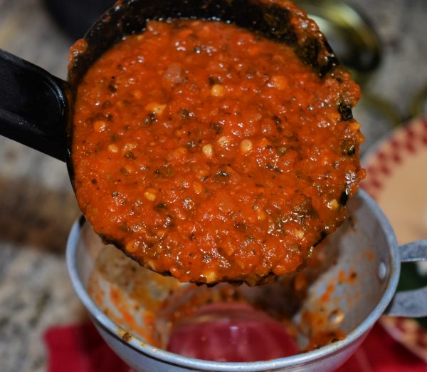Ladle of fresh homemade spaghetti sauce being poured into quart jar 