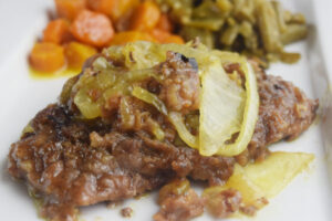 Freshly cooked cube steak smothered with onions on a white plate with green beans and carrots