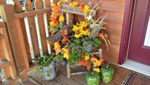 vivid fall colors of yellow, orange, green, etc in a floral display on a front porch with an old antique chair