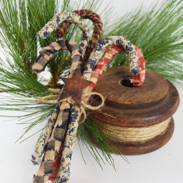 5 colorful rustic candy canes tied with a jute bow and rusty star laying on an old wooden spool