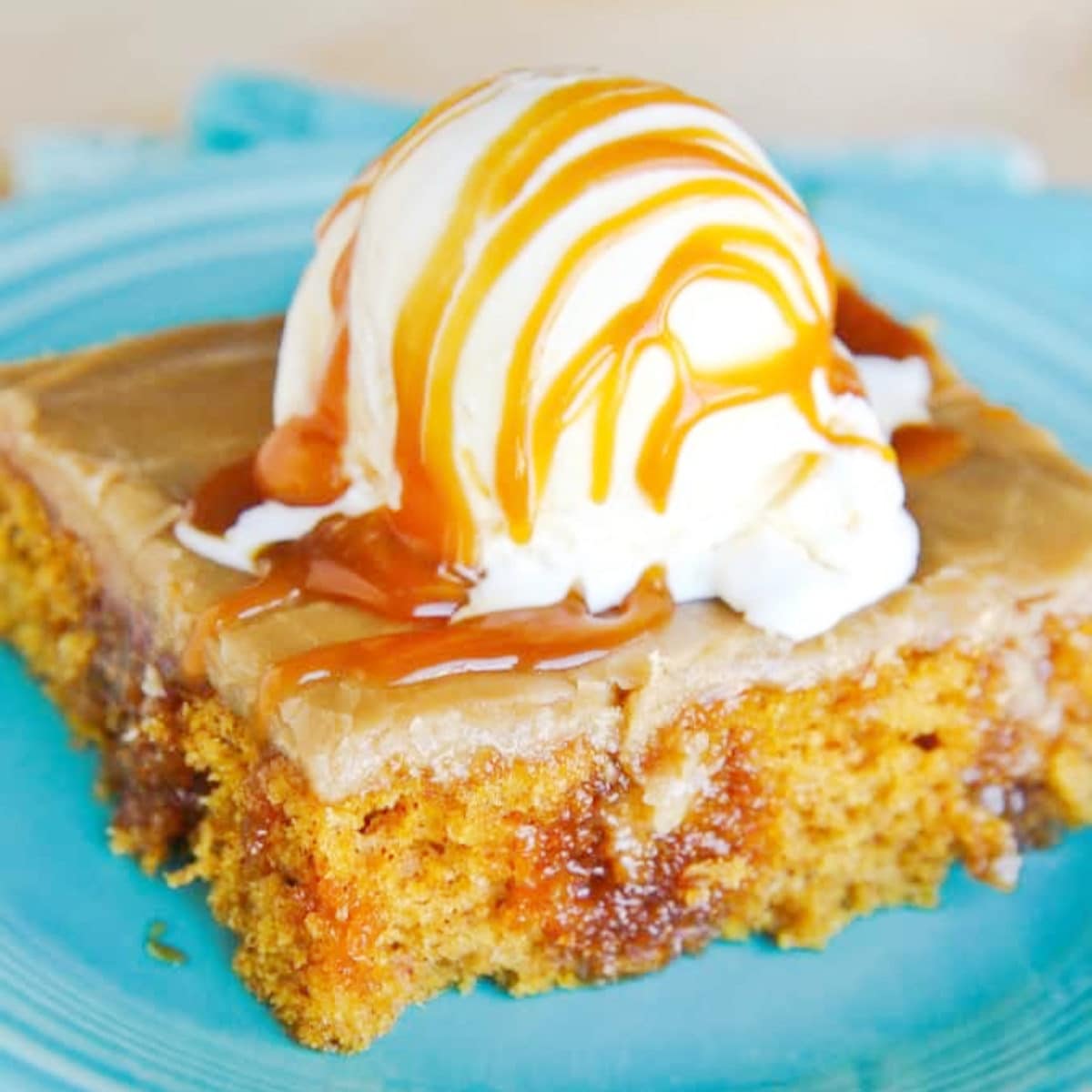 a slice of pumpkin poke cake on a turquoise plate with scoop of vanilla icecreams drizzled in caramel