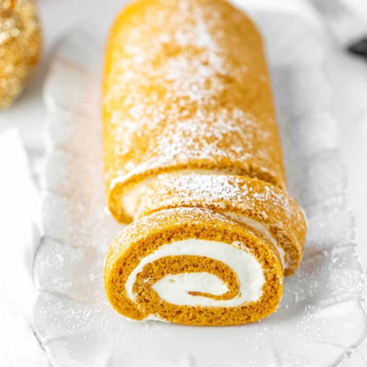 Pumpkin roll filled with cream chease and topped with sprinkled powdered sugar on a white plate.