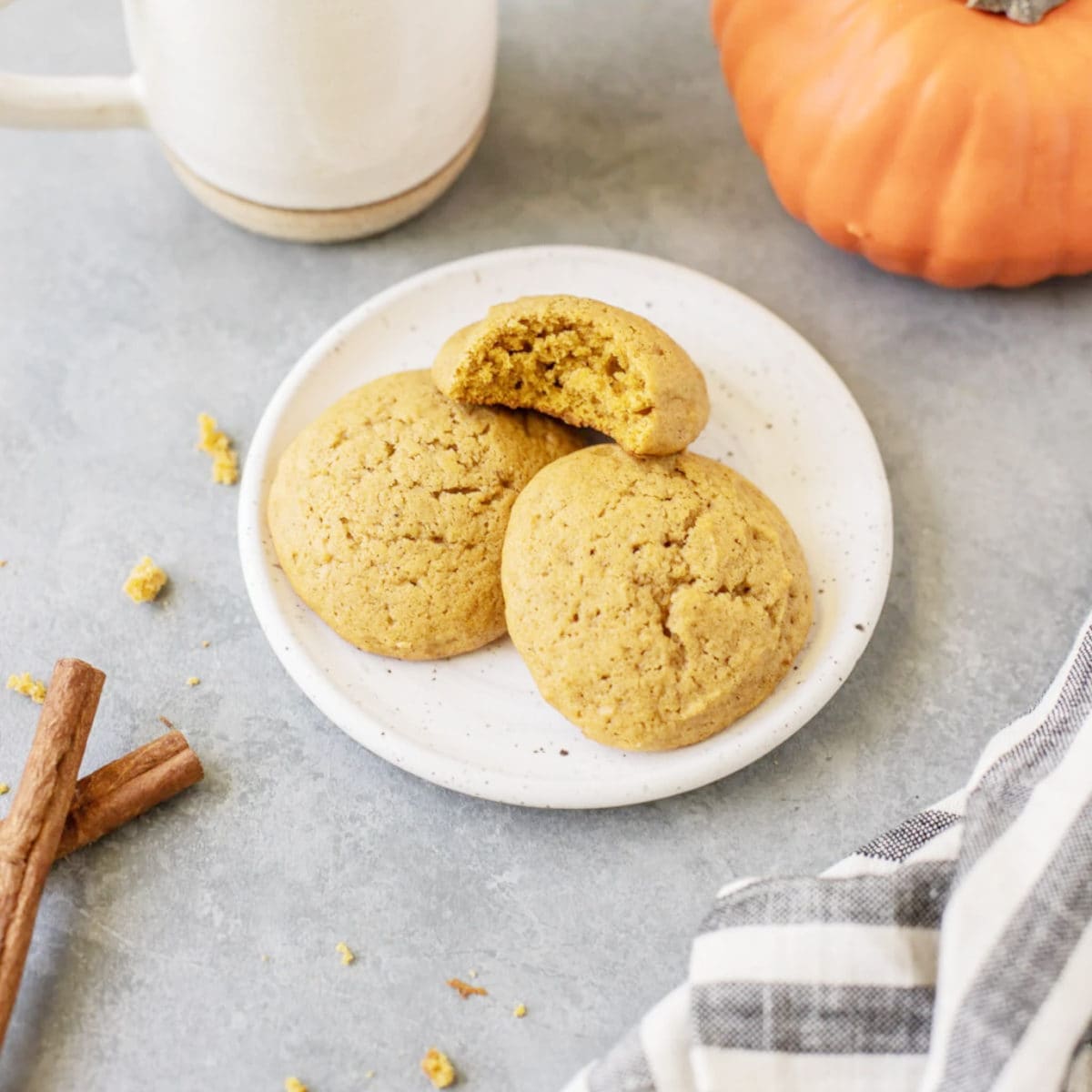 Three pumpkin cookies laying on a white plate, one has a bite taken out of it