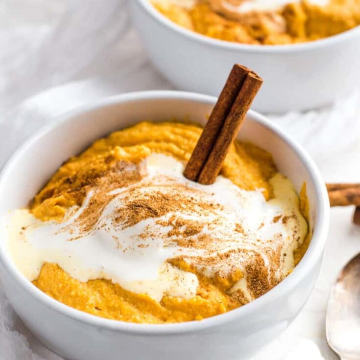 Pumpkin pudding in a white bowl with a stick of cinnamon.