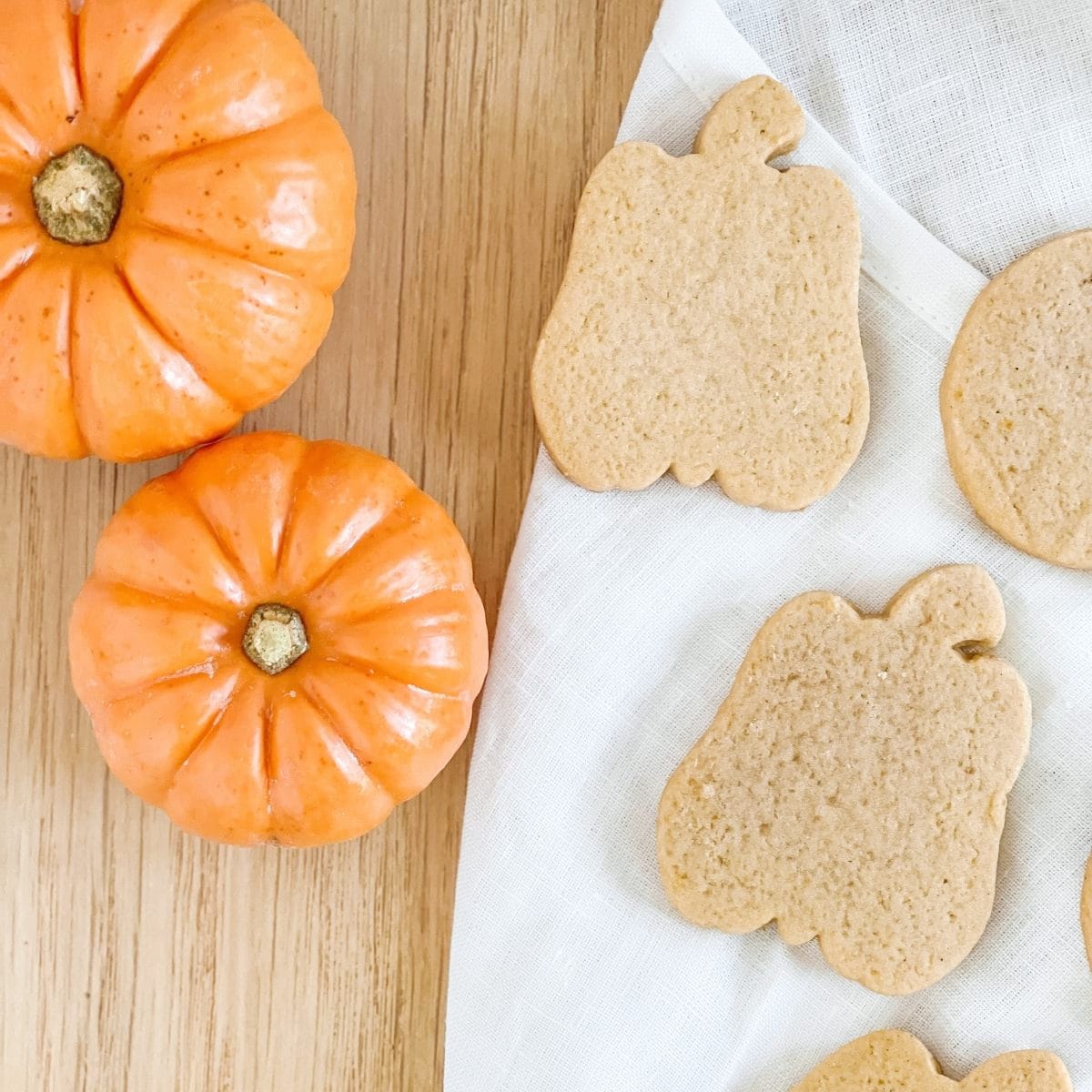 2 cute pumpkin shaped cookies laying on a white towel near 2 miniature pumpkins