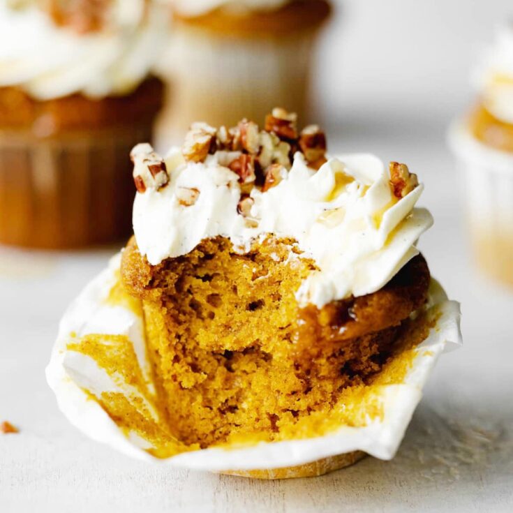 Fluffy and moist vegan pumpkin cupcake topped with vegan cream cheese frosting, maple syrup, and pecans.