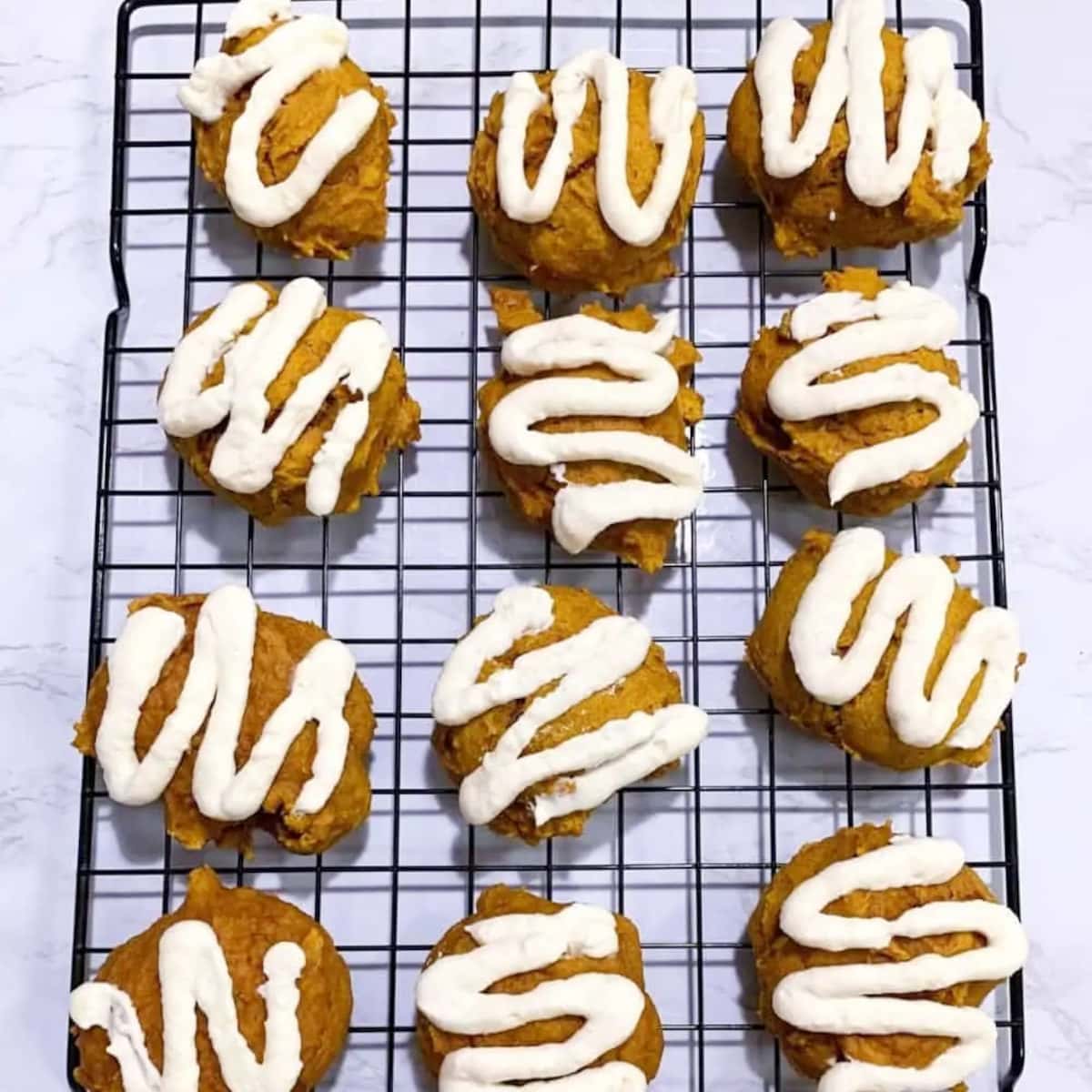 twelve pumpkin cookies with swirls of icing on a baking rack
