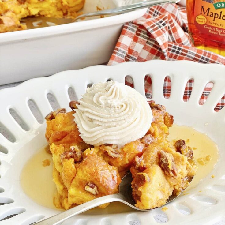 Pumpkin brioche bread pudding in a white bowl topped with pumpkin custard, raisins, and pecans.