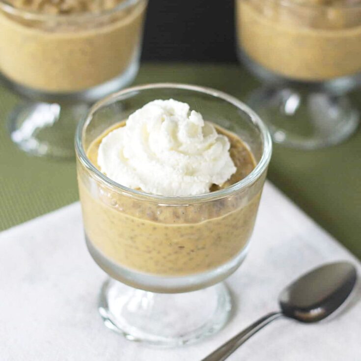 Pumpkin chia pudding with whipped cream topping in a clear bowl on a white napkin.