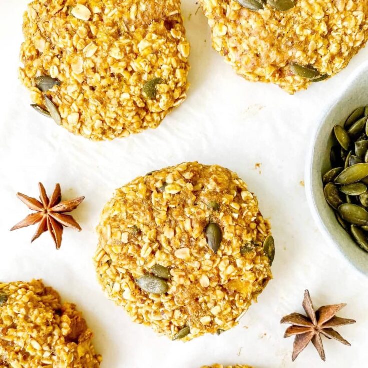 pumpkin cookies laying on a white surface with anise spices and green pumpkin seeds