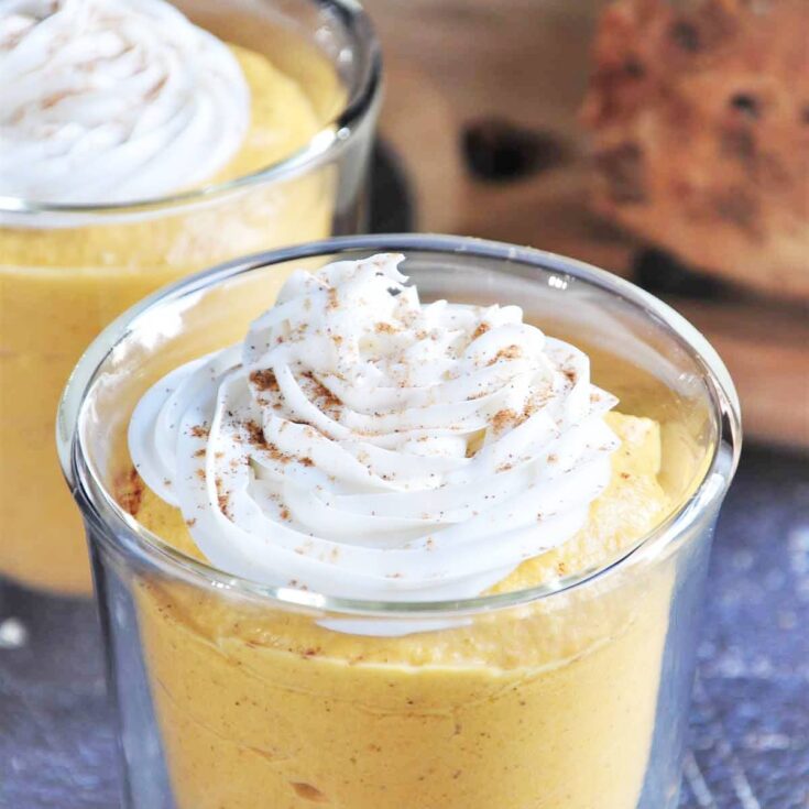 Pumpkin mousse in a clear cup with whip cream and cinnamon topping.