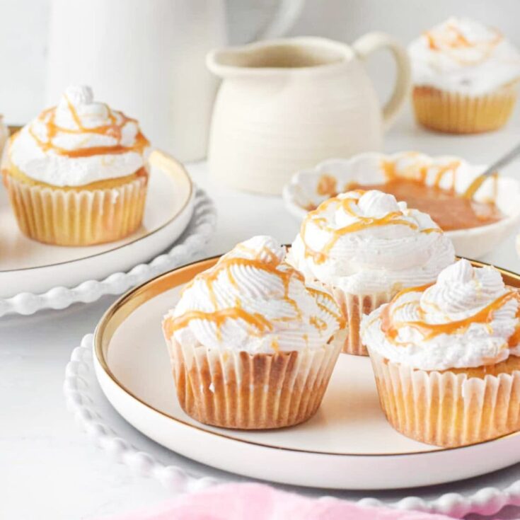 Pumpkin spice cupcakes topped with whip cream and caramel drizzle on a white plate.
