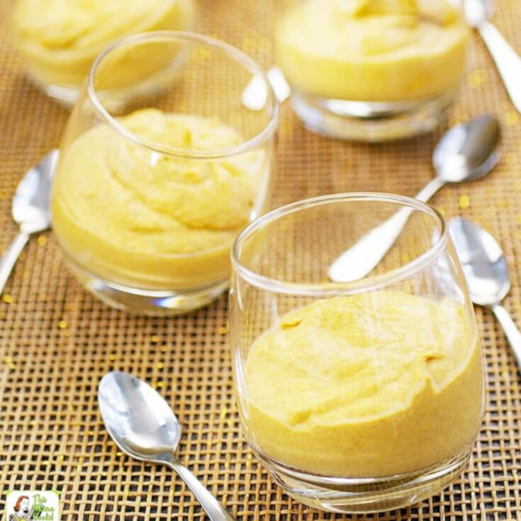 Pumpkin mousse in clear cups on a table with spoons.