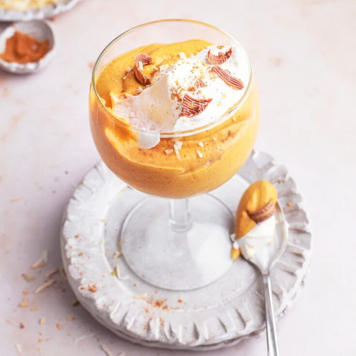 creamy pumpkin mousse in a stemmed glass topped with whipcream and nuts