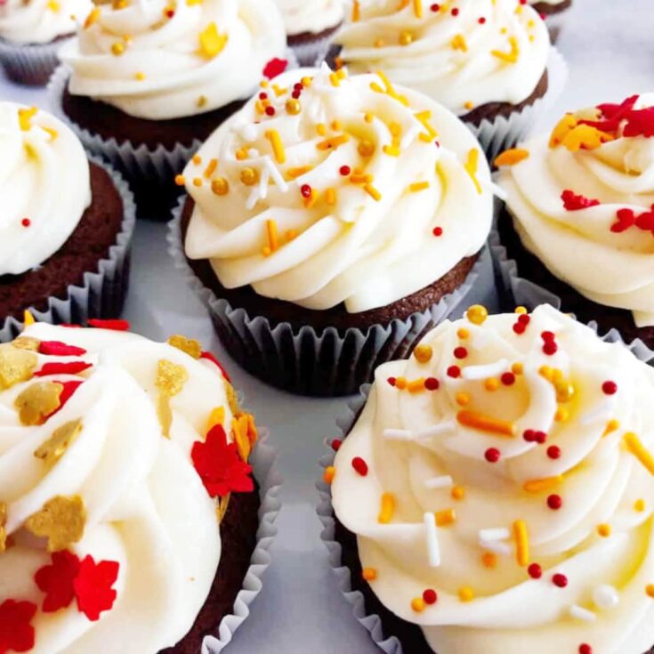 pumpkin cupcakes with white frosting and red sprinkles on top