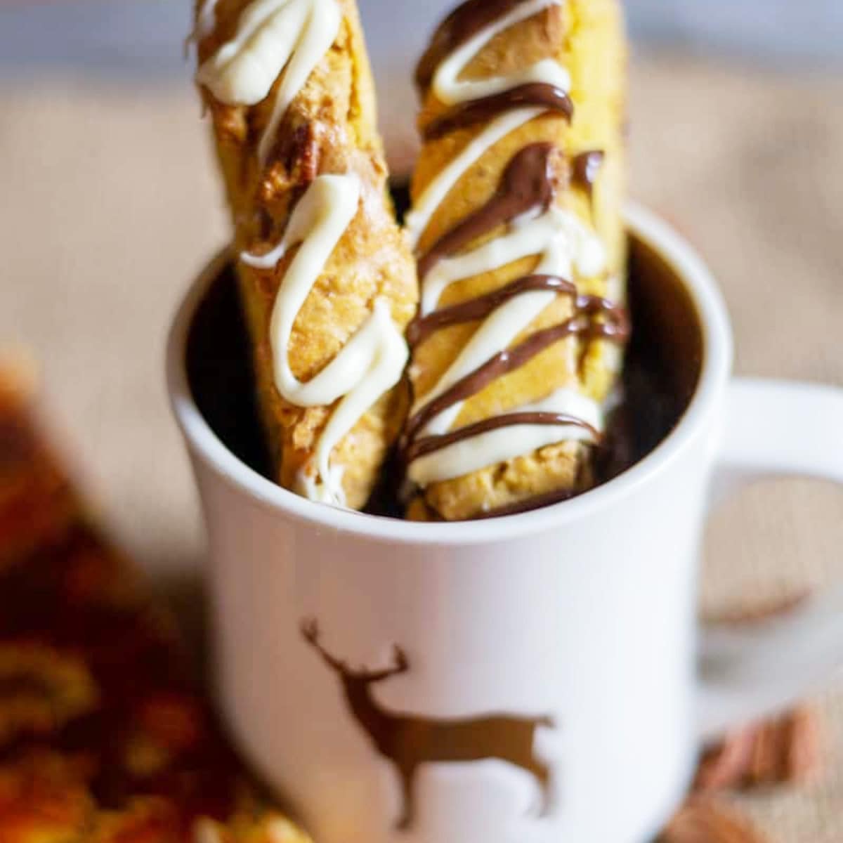 2 pumpkin biscotti cookies in a white mug swirled with white chocolate
