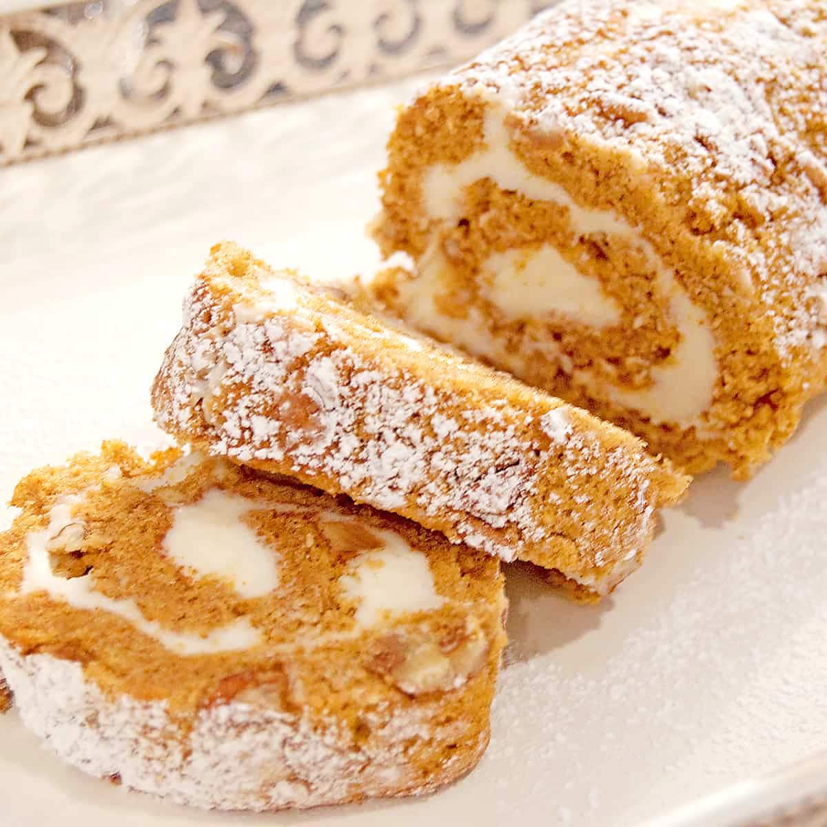 Pumpkin roll filled with cream cheese and topped with sprinkled powdered sugar on a white plate.