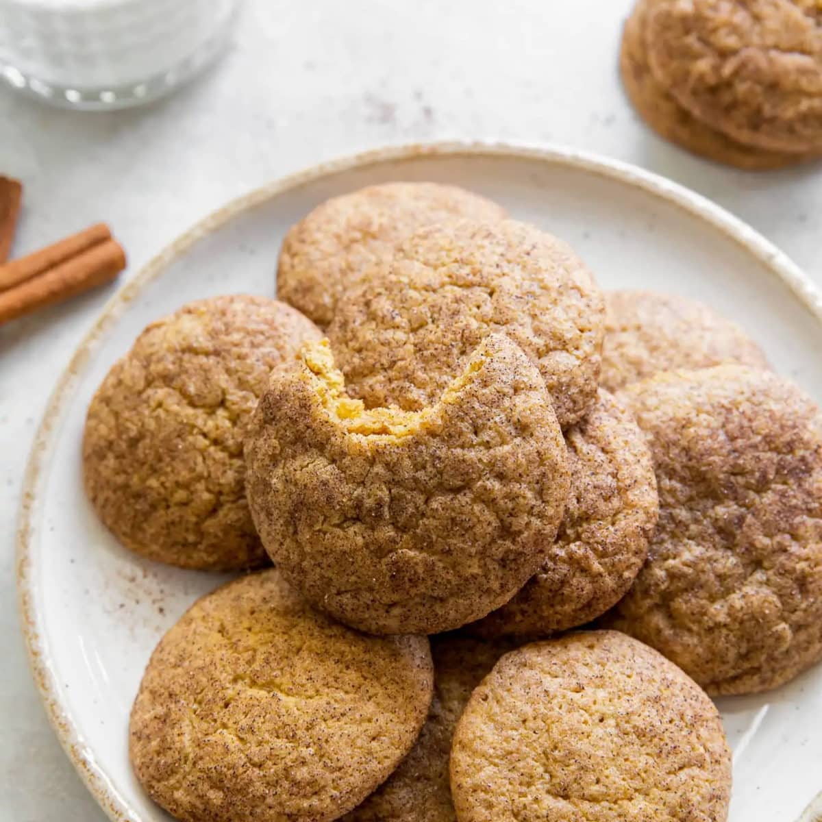 pumpkin cookies laying on a white plate with a gold edge next to two cinnamon sticks