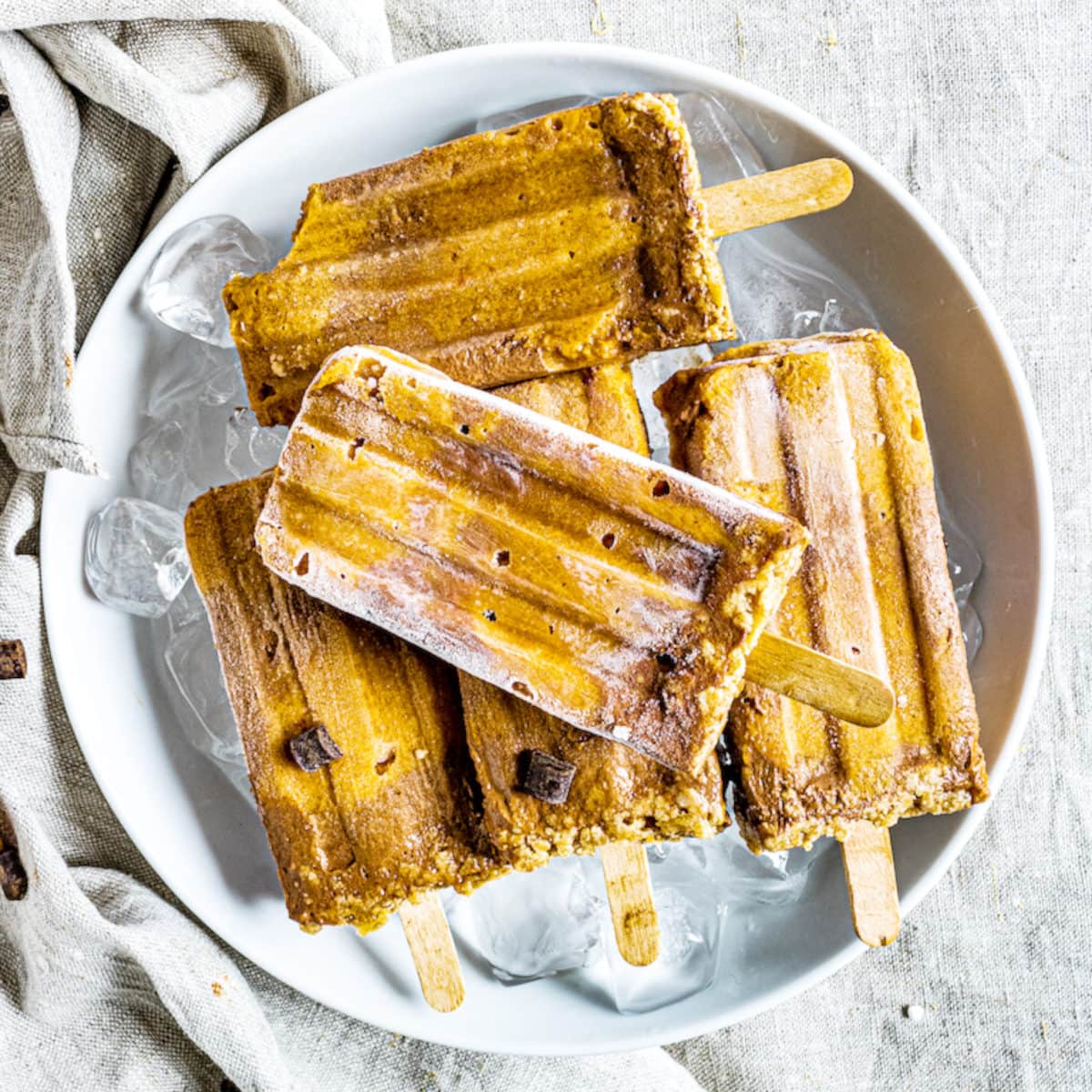 Five frozen chocolate pumpkin pie popsicles laying on a plate.