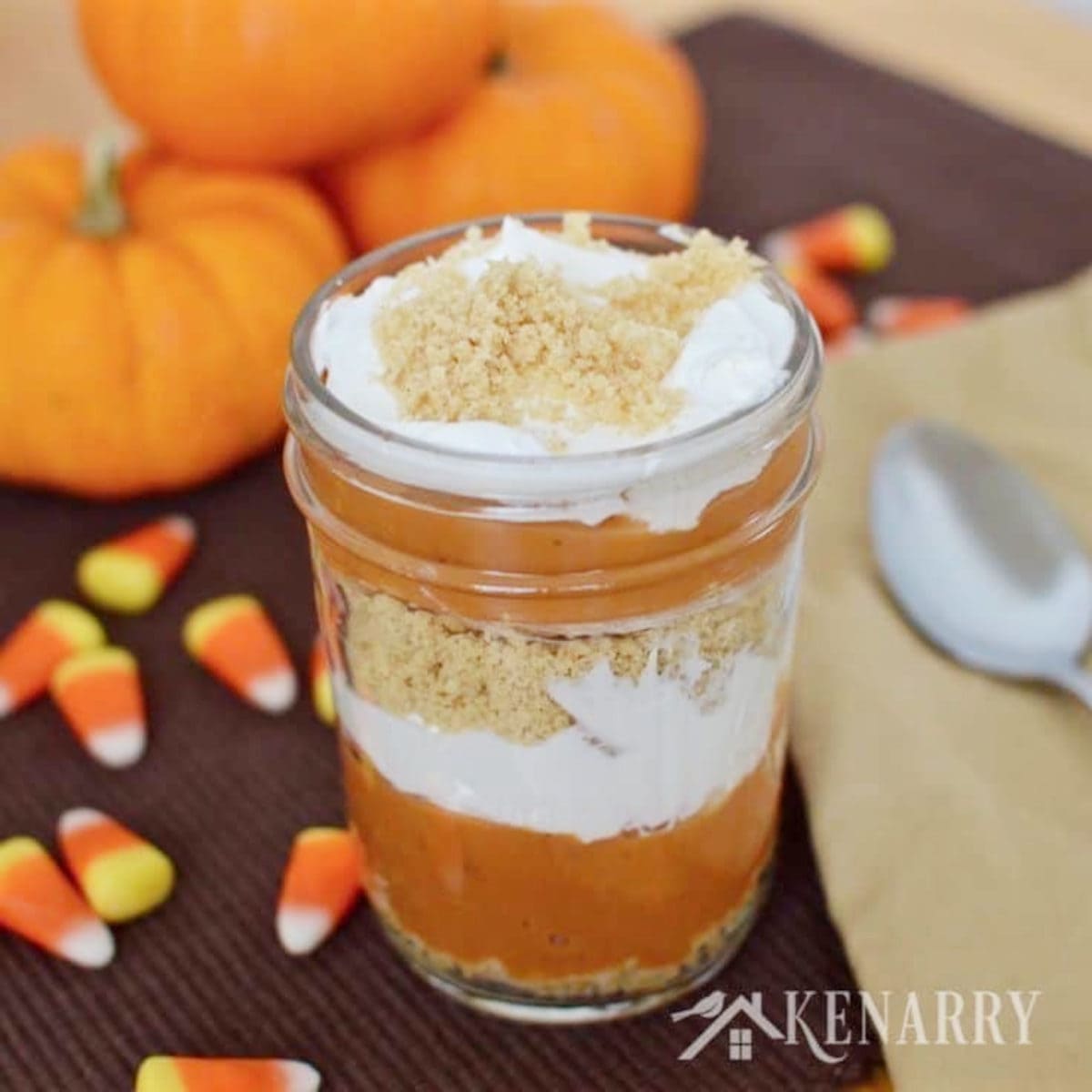 a colorful orange pumpkin ice cream parfait in a half pint mason jar with candy corn