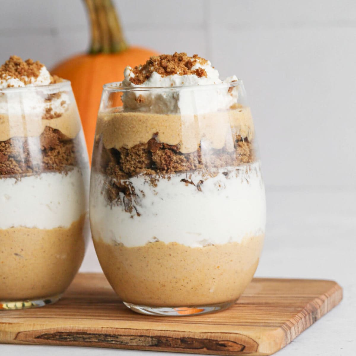 Pumpkin Gingersnap Parfaits in glass cups sitting on a wooden board.