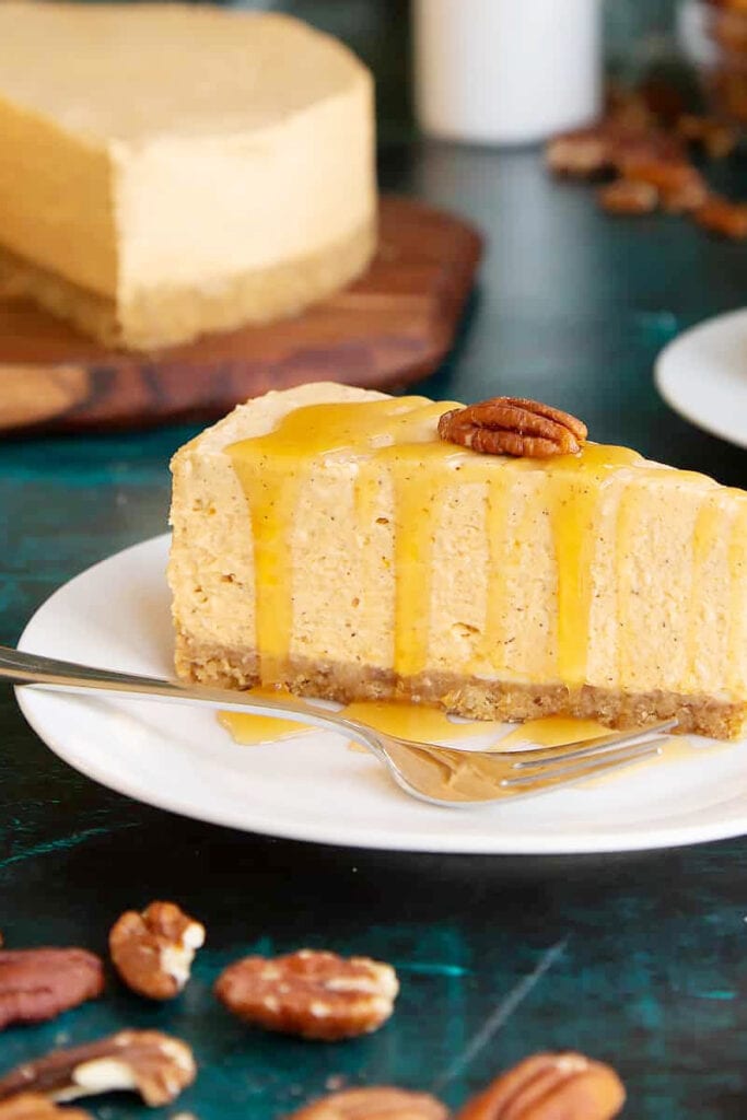 attractive slice of pumpkin cheesecake on a saucer with a fork and pecans