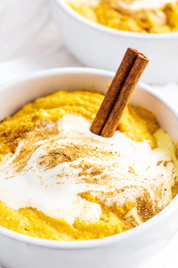 bowl of pumpkin pudding with sour cream and a cinnamon stick on top